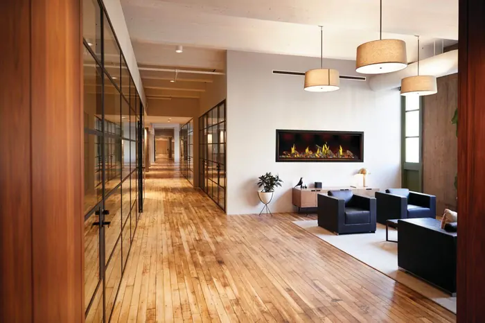 Napoleon Tall Linear Vector 74 gas fireplace with Luminous Logs set into a white wall in a bright lounge with wood floors