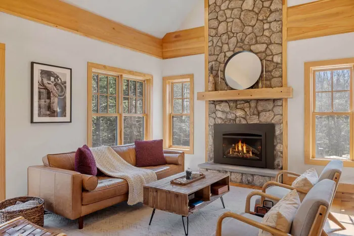 Napoleon gas insert with a black arched faceplate set into a fieldstone fireplace below a wood mantel, in a bright room with a leather sofa